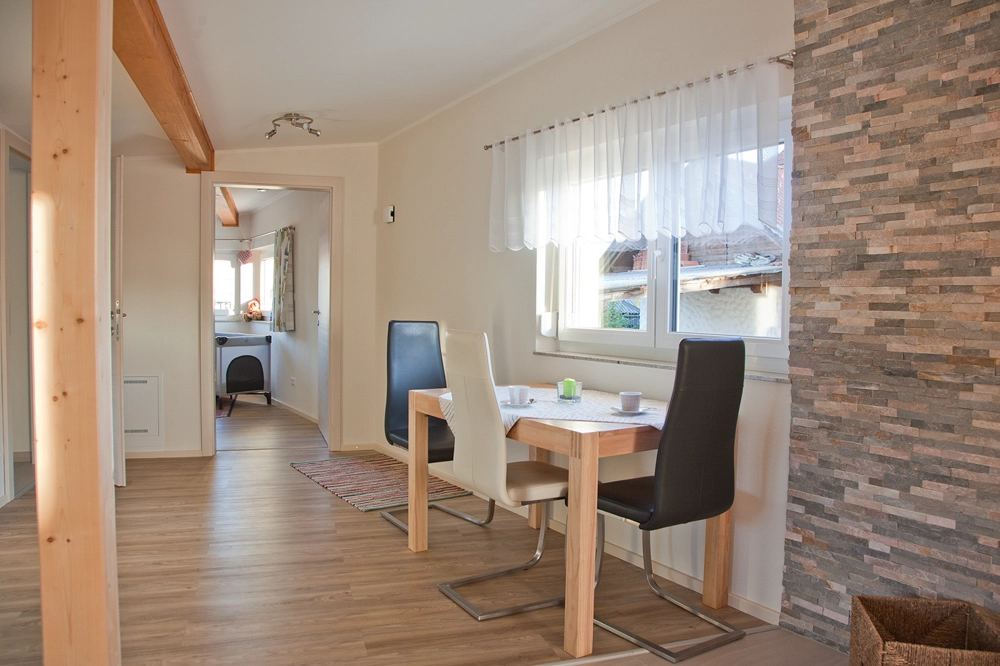 Ferienwohnung Greiler – Interiorfoto - Essbereicht mit Holztisch und 3 Stühlen in schwarz und weiß, großer Raum mit Holzbalken; klare Darstellung von Möbeln und Fläche, hell und freundlich.